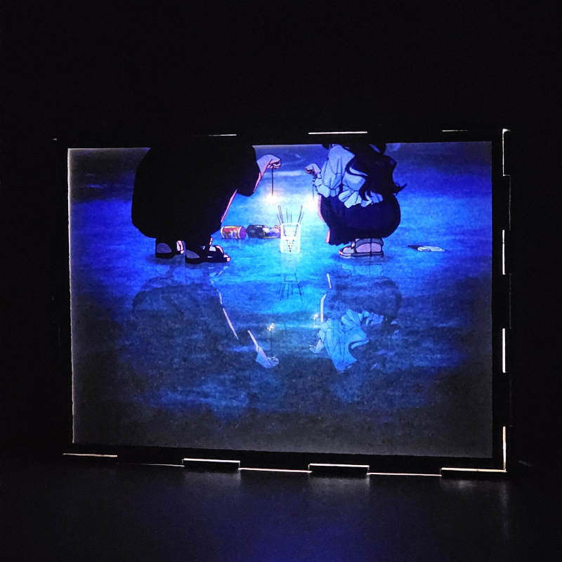 Lámpara ánime/manga  Kaoru Hana wa Rin to Saku  con doble imagen de la pareja Kaoruko Waguri y Rintaro Tsumugi, vista encendida, donde se revela la ilustración completa al encender la luz LED.