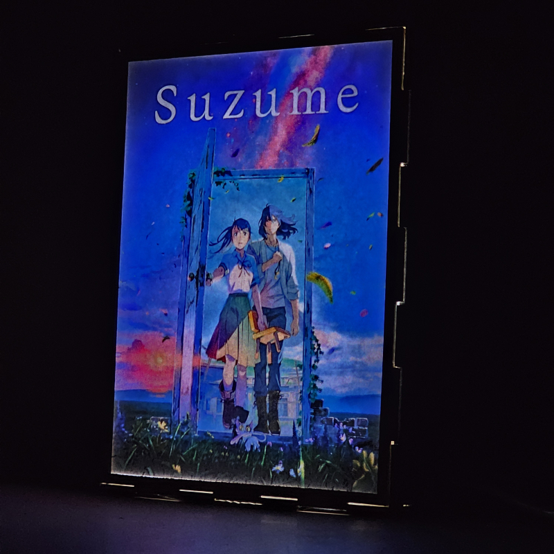 Lámpara ánime/manga  Suzume  con doble imagen del grupo Iwato Suzume, Sōta Munakata y Daijin, vista encendida, donde se revela la ilustración completa al encender la luz LED.