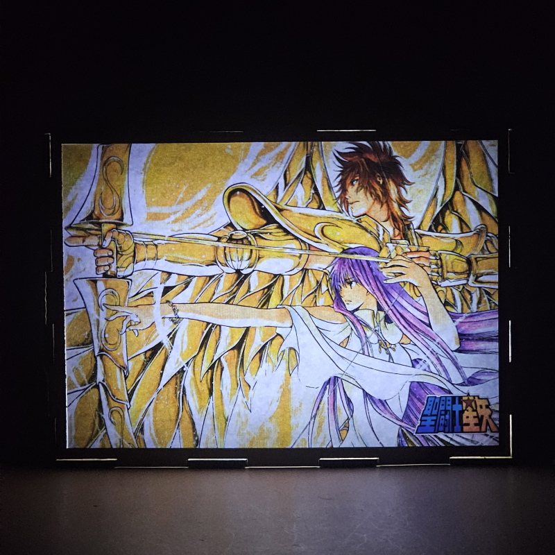 Lámpara ánime/manga  Los Caballeros del Zodiaco  con doble imagen del grupo Sísifo de Sagitario y Sasha, vista encendida, donde se revela la ilustración completa al encender la luz LED.
