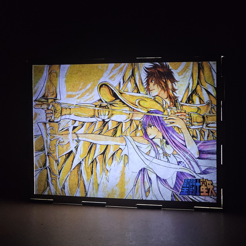 Lámpara ánime/manga  Los Caballeros del Zodiaco  con doble imagen del grupo Sísifo de Sagitario y Sasha, vista encendida, donde se revela la ilustración completa al encender la luz LED.