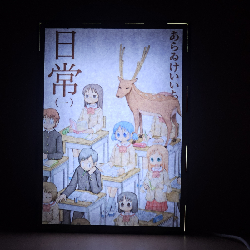 Lámpara ánime/manga  Nichijou  con doble imagen del grupo Yuuko Aioi, Sakamoto, Mai Minakami, Nano Shinonome, Mio Naganohara y Koujirou Sasahara, vista encendida, donde se revela la ilustración completa al encender la luz LED.
