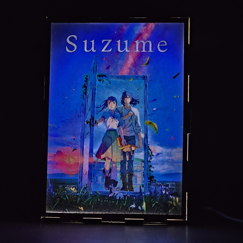 Lámpara ánime/manga  Suzume  con doble imagen del grupo Iwato Suzume, Sōta Munakata y Daijin, vista encendida, donde se revela la ilustración completa al encender la luz LED.