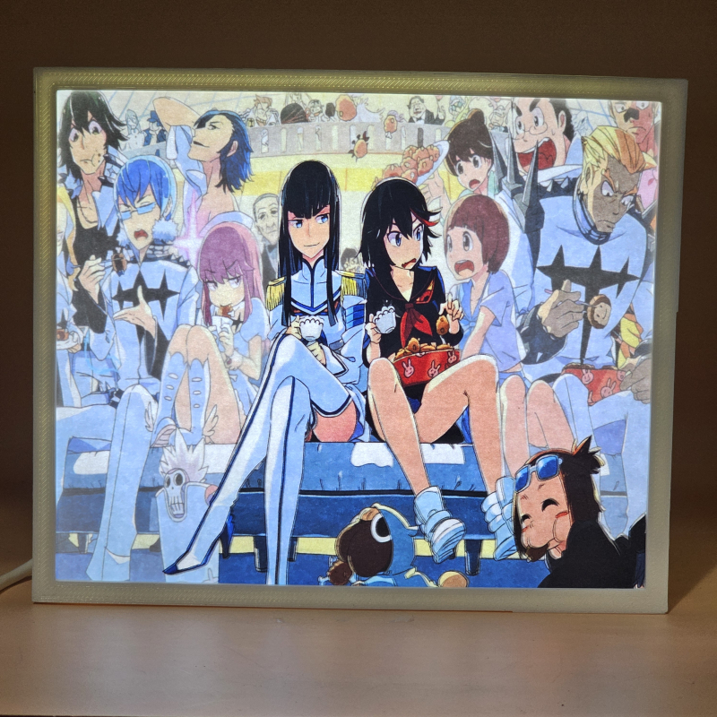 Lámpara ánime/manga  Kill la Kill  con doble imagen del grupo Ryuko Matoi, Satsuki Kiryūin, Mako Mankanshoku, Senketsu, Nonon Jakuzure, Ira Gamagōri, Mataro Mankanshoku, Houka Inumuta, Aikurō Mikisugi, Uzu Sanageyama, Tsumugu Kinagase, Barazo Mankanshoku y Mitsuzō Soroi, vista encendida, donde se revela la ilustración completa al encender la luz LED.