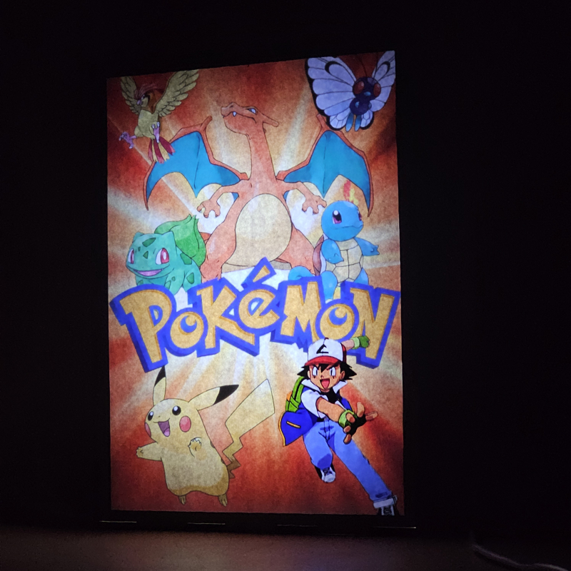 Lámpara ánime/manga  Pokémon  con doble imagen del grupo Ash Ketchum y Pikachu, vista encendida, donde se revela la ilustración completa al encender la luz LED.