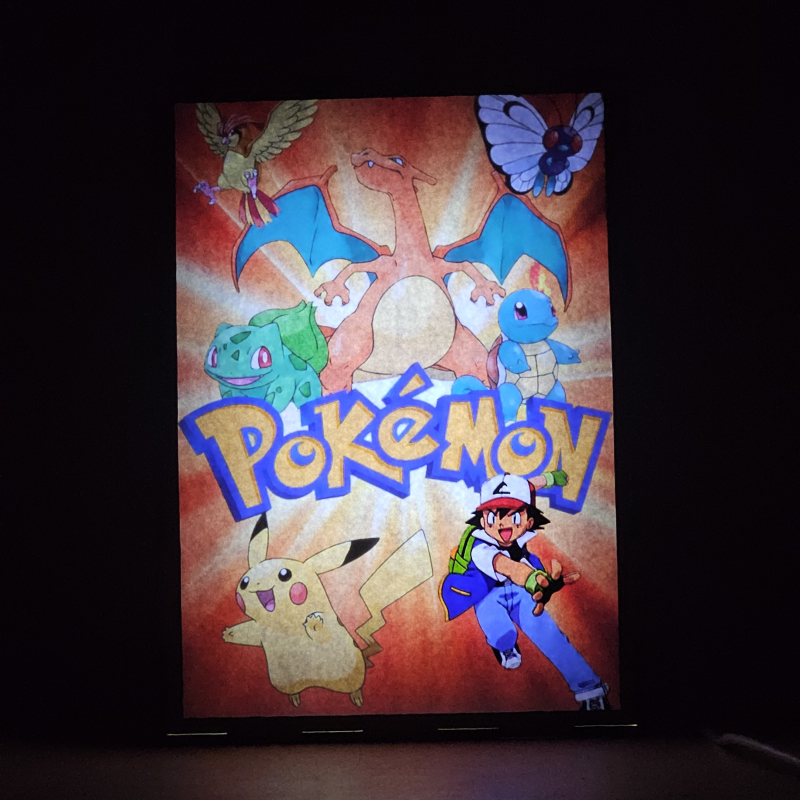 Lámpara ánime/manga  Pokémon  con doble imagen del grupo Ash Ketchum y Pikachu, vista encendida, donde se revela la ilustración completa al encender la luz LED.